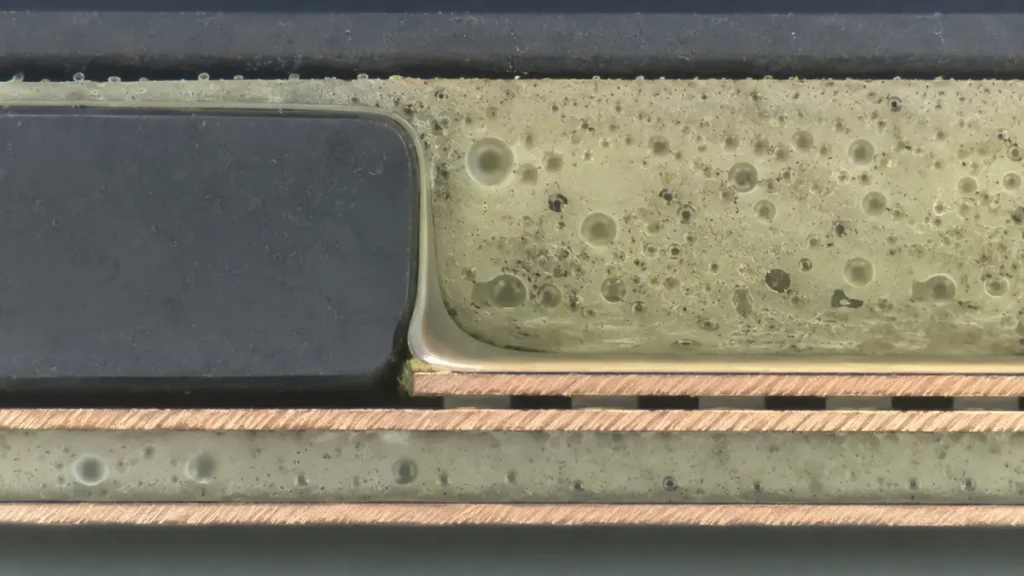 Metallographic microsection of an embedded component PCB showing resin voids and dielectric air bubbles near the component corner.
